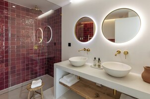 Casa de banho moderna com lavatório branco, duas espelhas redondas, uma grande pia branca e um chuveiro com parede em azulejos vermelhos.