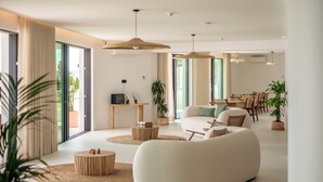 A modern living room with a large sofa, a coffee table, and a dining area with chairs and a table. - Villa Loreto (Olhao)