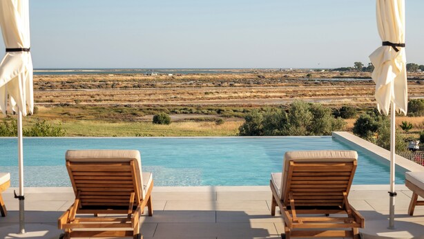 A poolside area with two wooden lounge chairs and white umbrellas, overlooking a vast landscape. - Villa Loreto (Olhao)