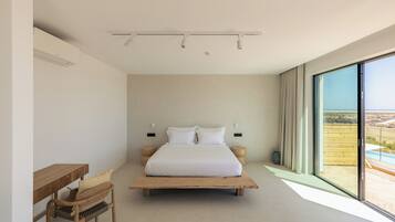 A modern bedroom with a large bed, a wooden desk, and a view of the outdoors.