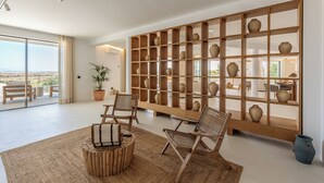 A spacious living area with a large wooden bookshelf, two wicker chairs, a round coffee table, and a view of the outdoors. - Villa Loreto (Olhao)