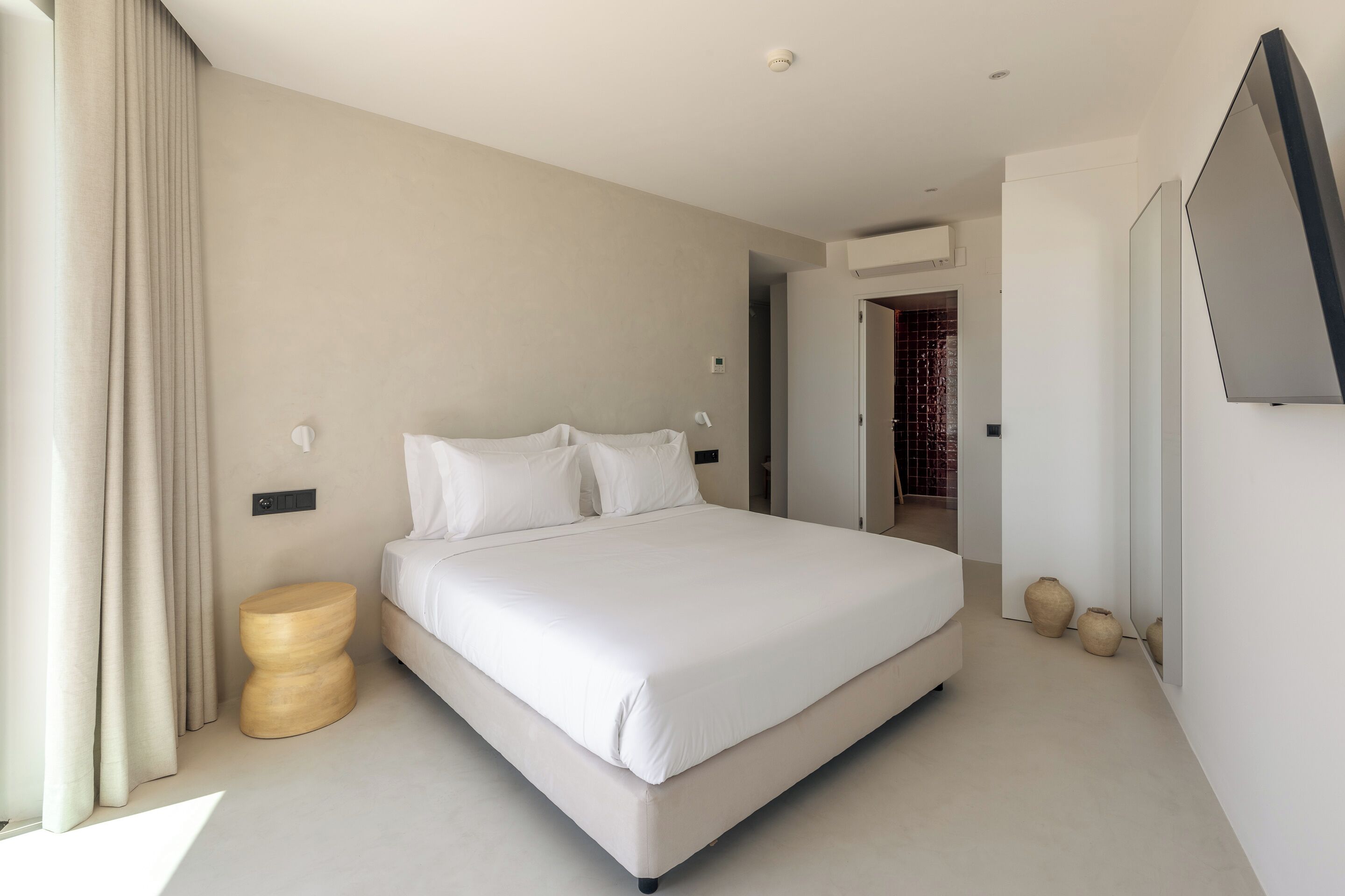 A modern bedroom with a large bed, a bedside table, and a flat-screen TV mounted on the wall.