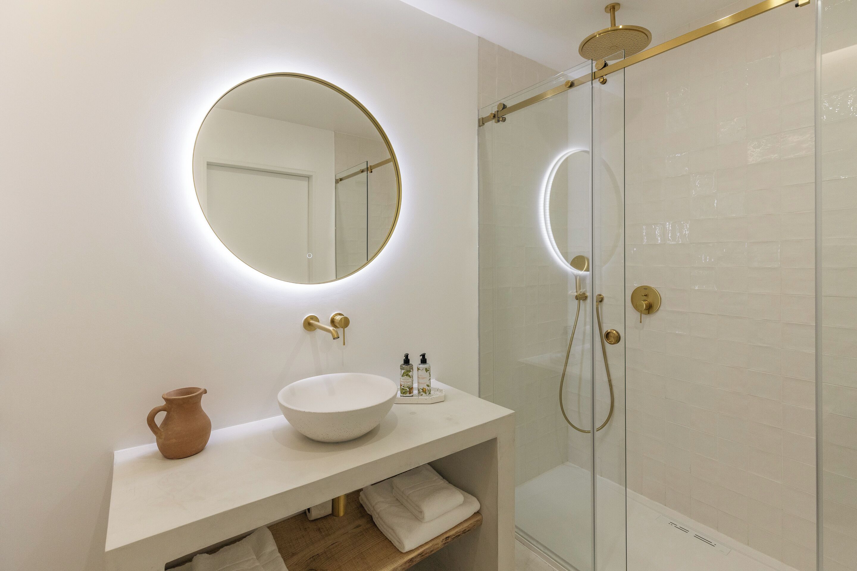 A modern bathroom with a round mirror, white sink, and a glass-enclosed shower.