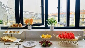 A breakfast setup with pastries, fruit, and bread on a table by a large window with a city view. - Qianxun Intelligent Hotel Haiyisu (Qibala International Resort) (Menghai)
