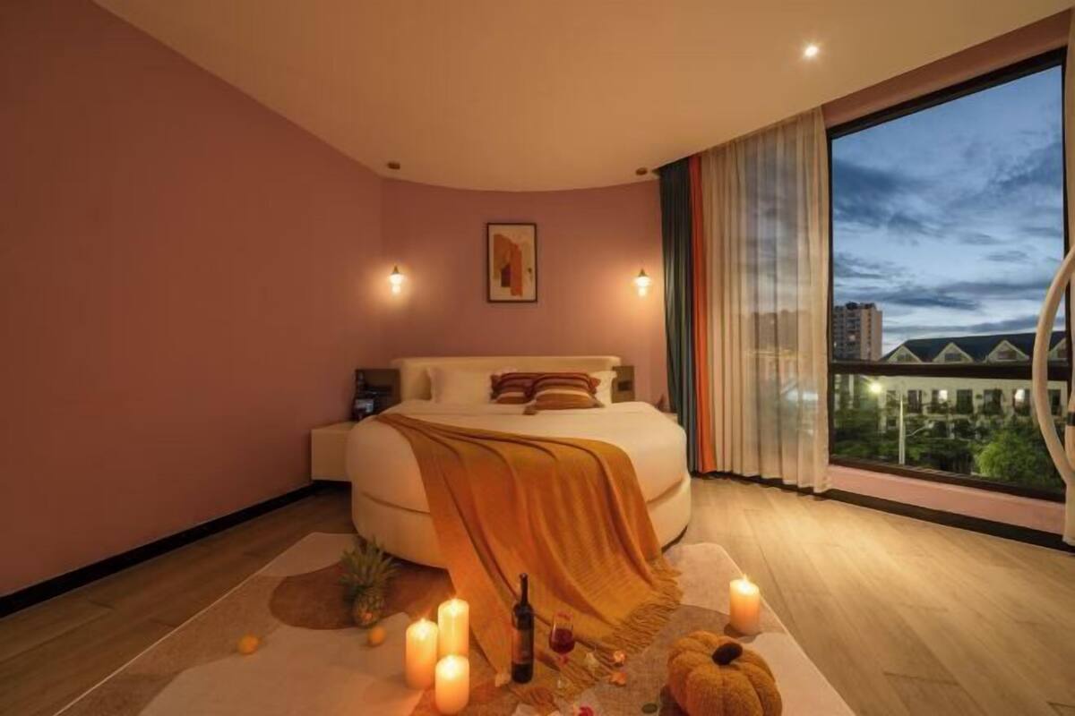 A modern bedroom with a large bed, a view of the cityscape, and a city skyline visible through the window.