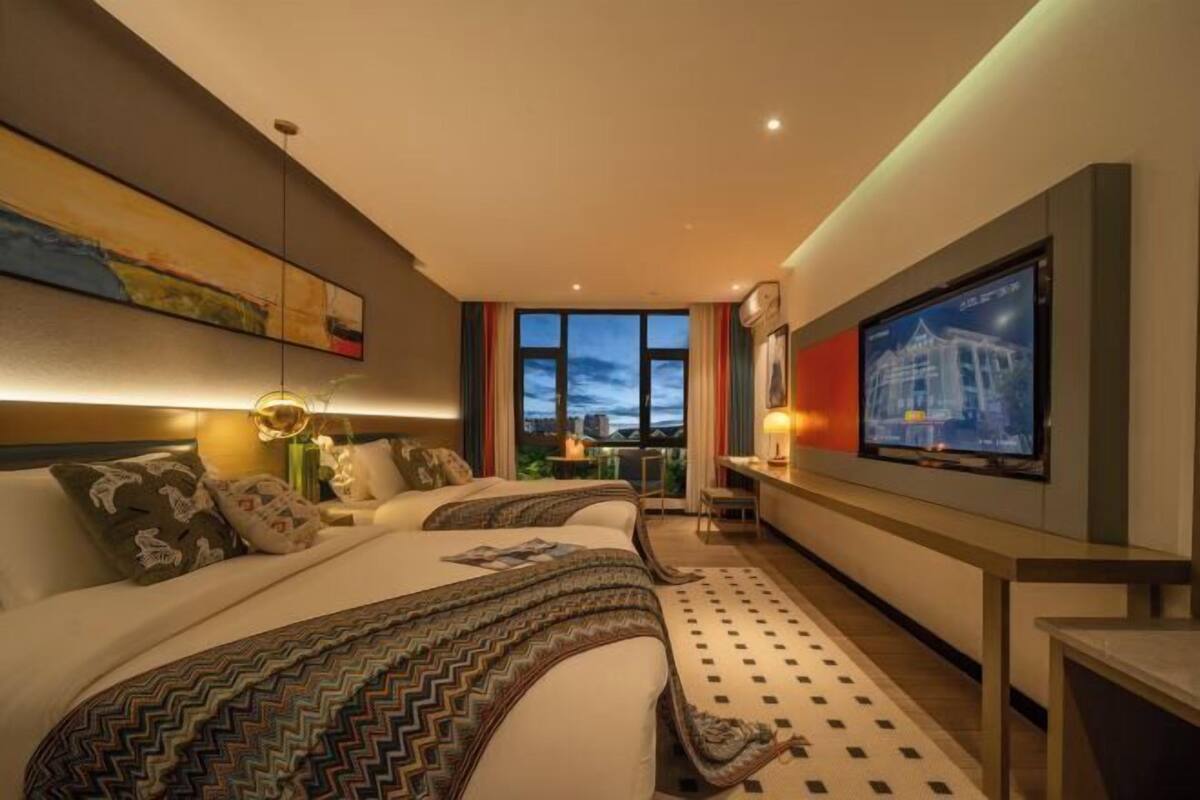 A hotel room with two beds, a TV, a desk, and a view of the cityscape.