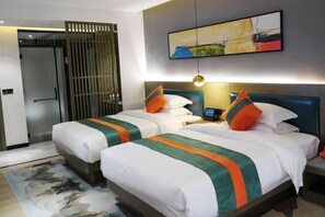 A hotel room with two beds, each with white bedding and green and orange accents. There is a painting on the wall above the beds, a small table with a lamp, and a sliding door in the background. - Qianxun Intelligent Hotel Haiyisu (Qibala International Resort) (Menghai)