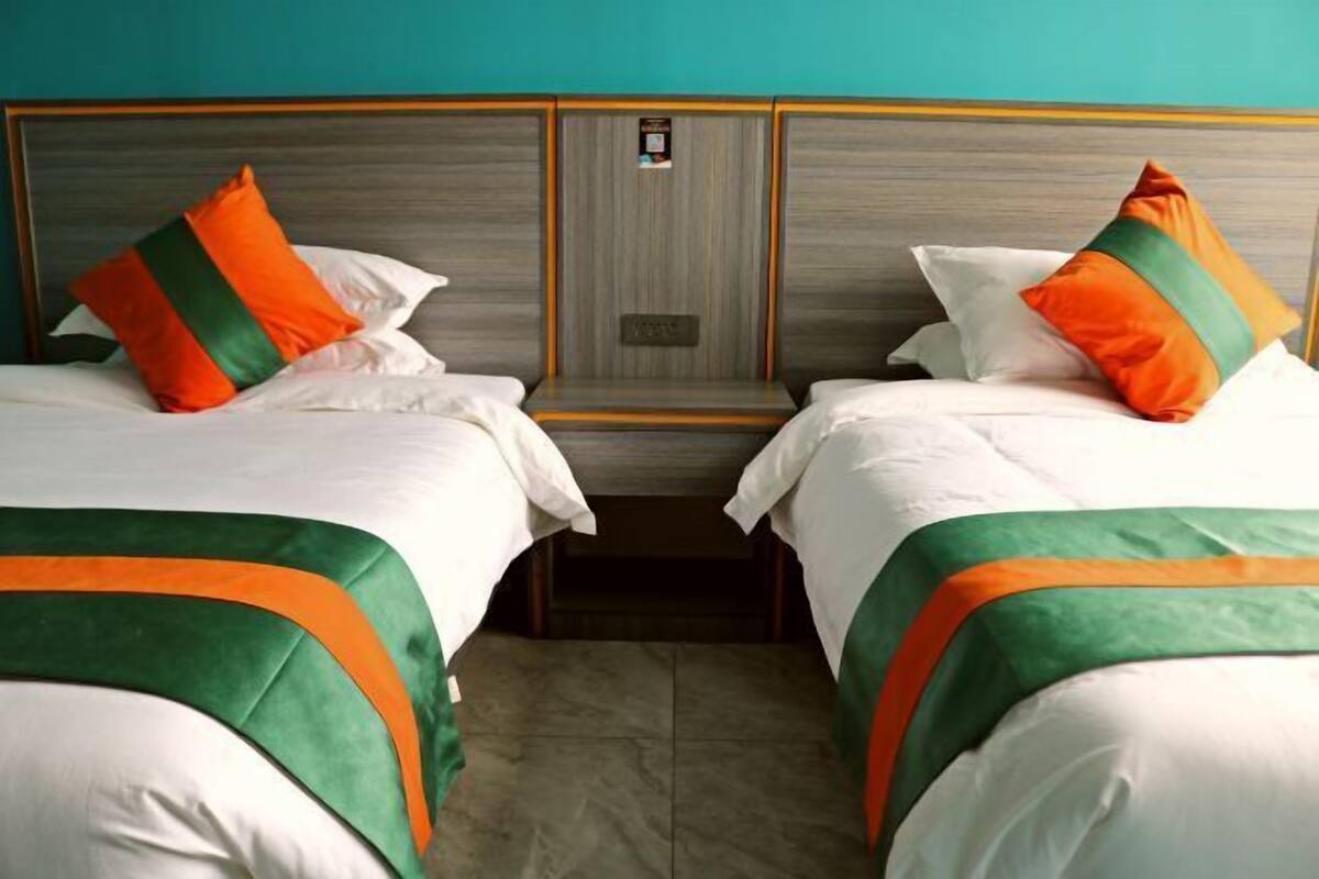 A hotel room with two beds, each with white bedding and orange and green pillows.