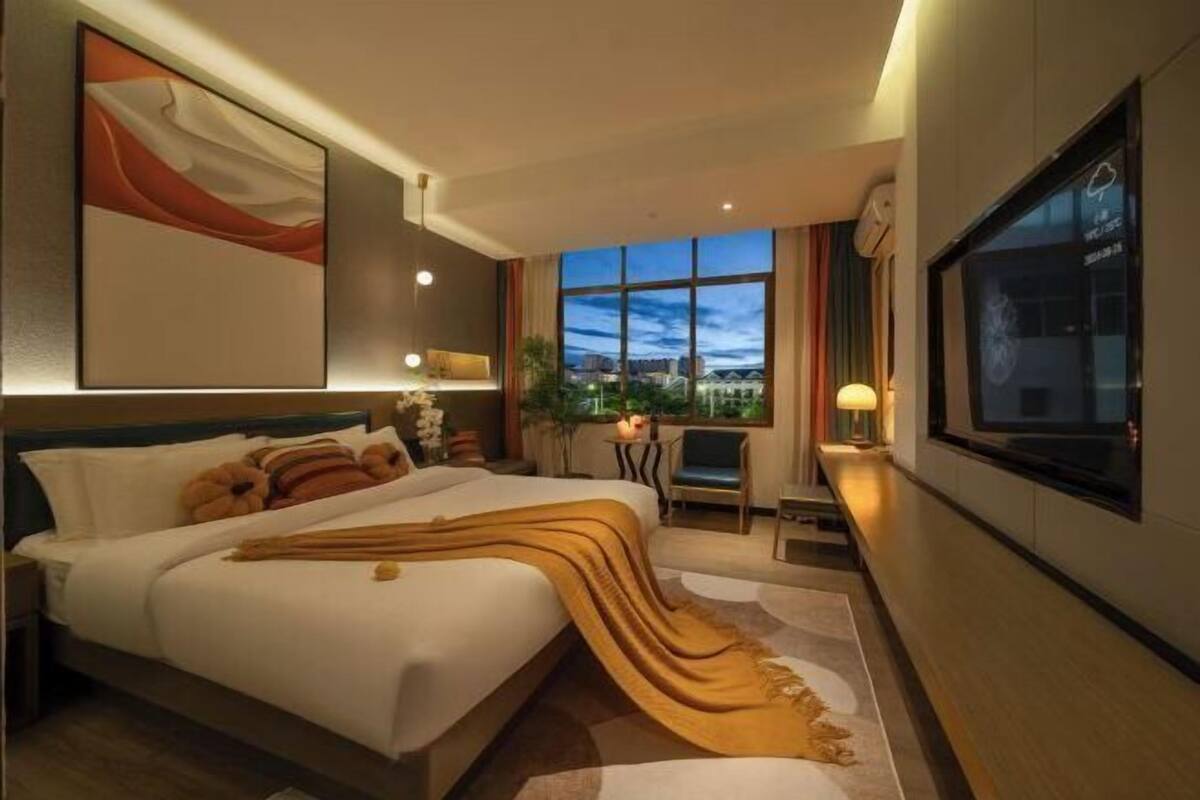 A hotel room with a large bed, a TV, a desk, and a view of the cityscape.