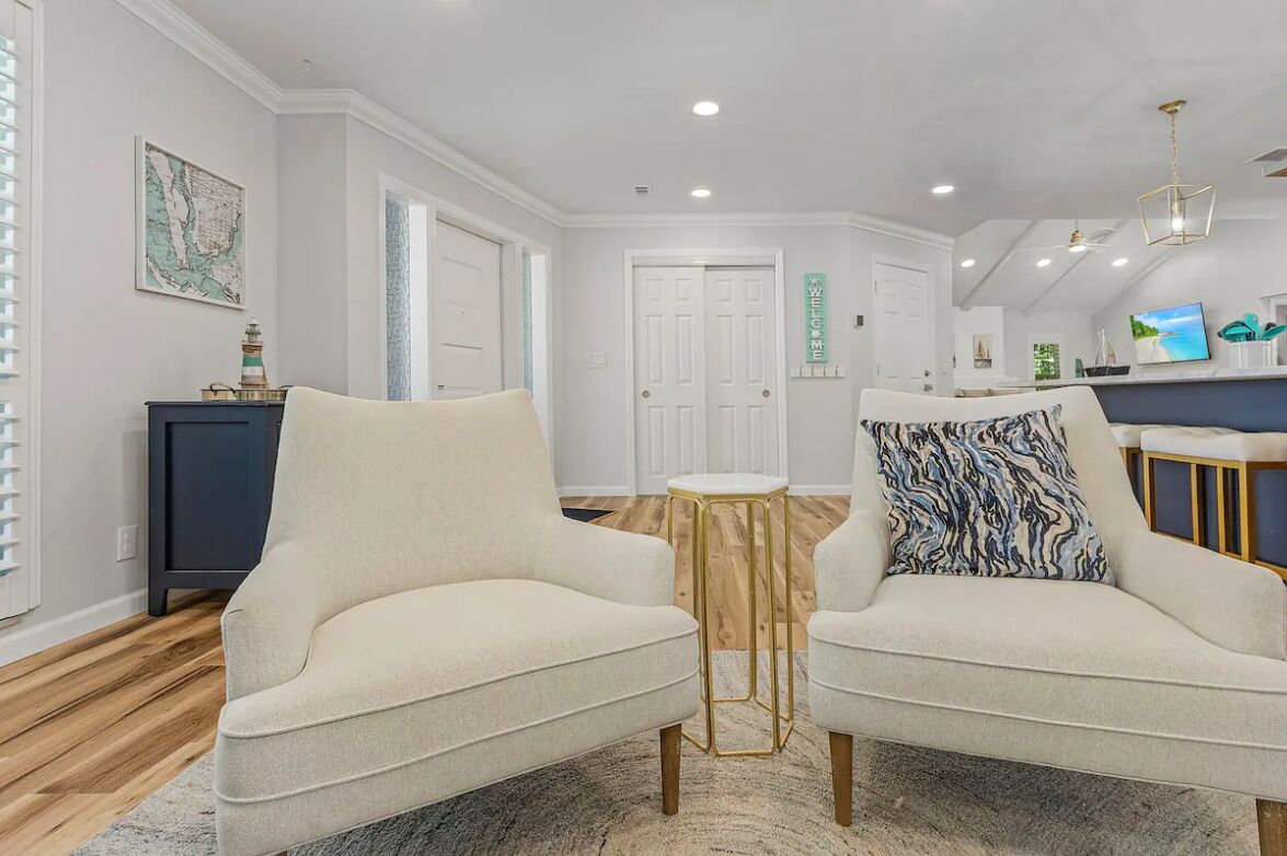 A modern living room with two cream-colored armchairs, a small round table, and a patterned throw pillow.