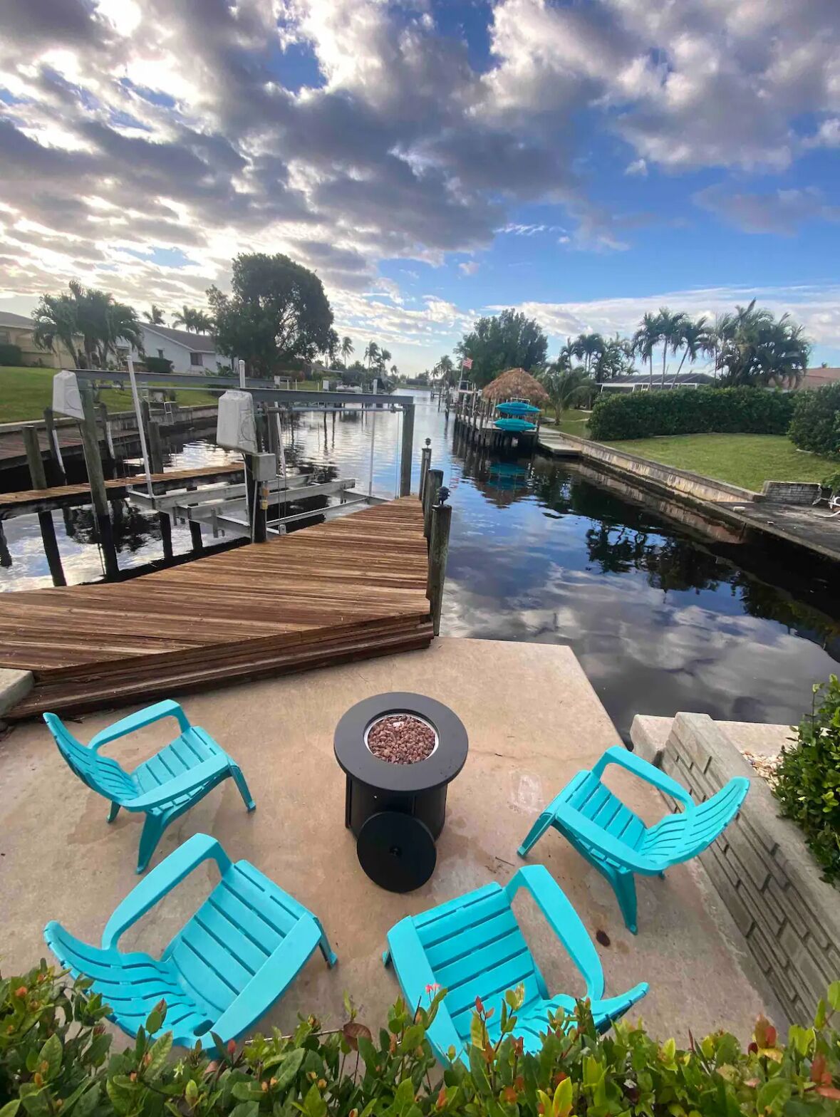 A dock with a wooden deck and a small round table with a fire pit in the center, surrounded by four turquoise chairs.