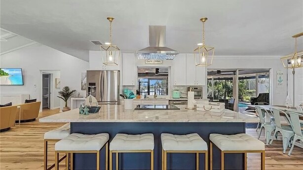 Una cocina moderna con una isla central, taburetes de bar, iluminación colgante y vistas al exterior.