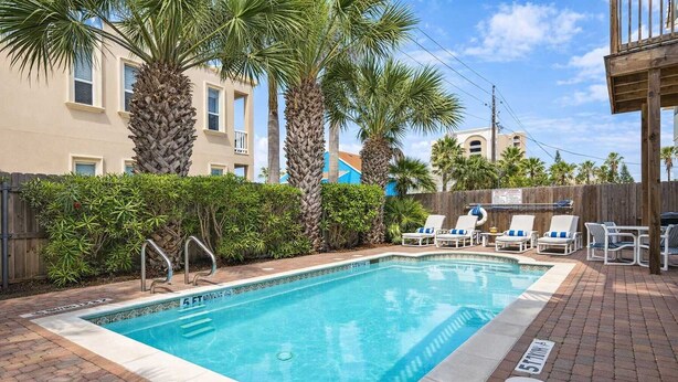Une piscine rectangulaire bordée de carreaux, entourée de palmiers et d’une clôture en bois.