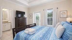 Une chambre à coucher avec un lit, une commode, un téléviseur et une fenêtre avec des rideaux.