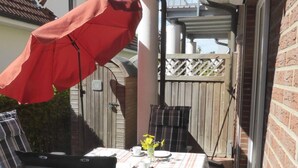 Terrassa exterior amb taula preparada per a dues persones, un parasol vermell i una tanca de fusta.