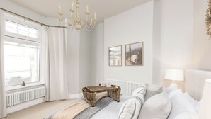 Un dormitorio con cama, mesita de noche, lámpara, radiador y ventana con cortinas.