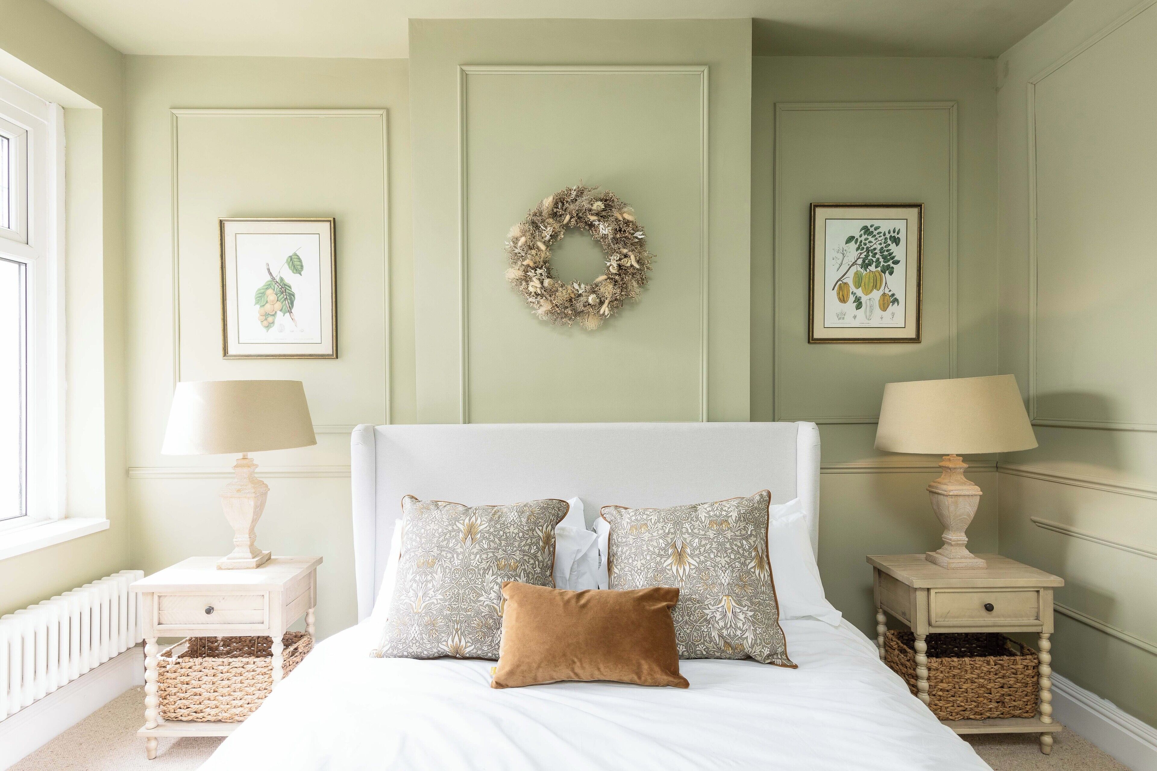 A neatly arranged bedroom with a bed, two bedside tables with lamps, and framed botanical prints on the walls.