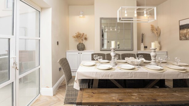 Comedor con una mesa dispuesta para cuatro, una lámpara colgante y un ventanal grande.