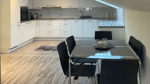 A modern kitchen with white cabinets, a dining table with chairs, and a view of the city through a large window. - Baba Apart 1 Große, Moderne Wohnung Direkt an der Schweizer Grenze (Laufenburg)