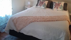 A bedroom with a bed, a nightstand, a lamp, and a window with curtains.