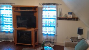 A living room with a TV, wooden entertainment unit, a coffee table with a plant, a sofa with cushions, and a lamp on a side table.