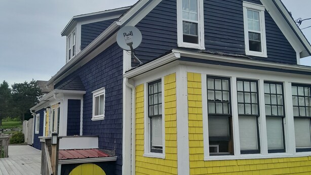 A two-story house with a blue roof and yellow siding, featuring a small porch and a yellow garage door.