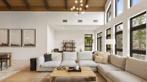 A spacious living room with a large sectional sofa, a coffee table, and a fireplace. There are large windows providing natural light and a view of the outdoors. - Tremblant Prestige - Verbier 12-203 (Mont-Tremblant)