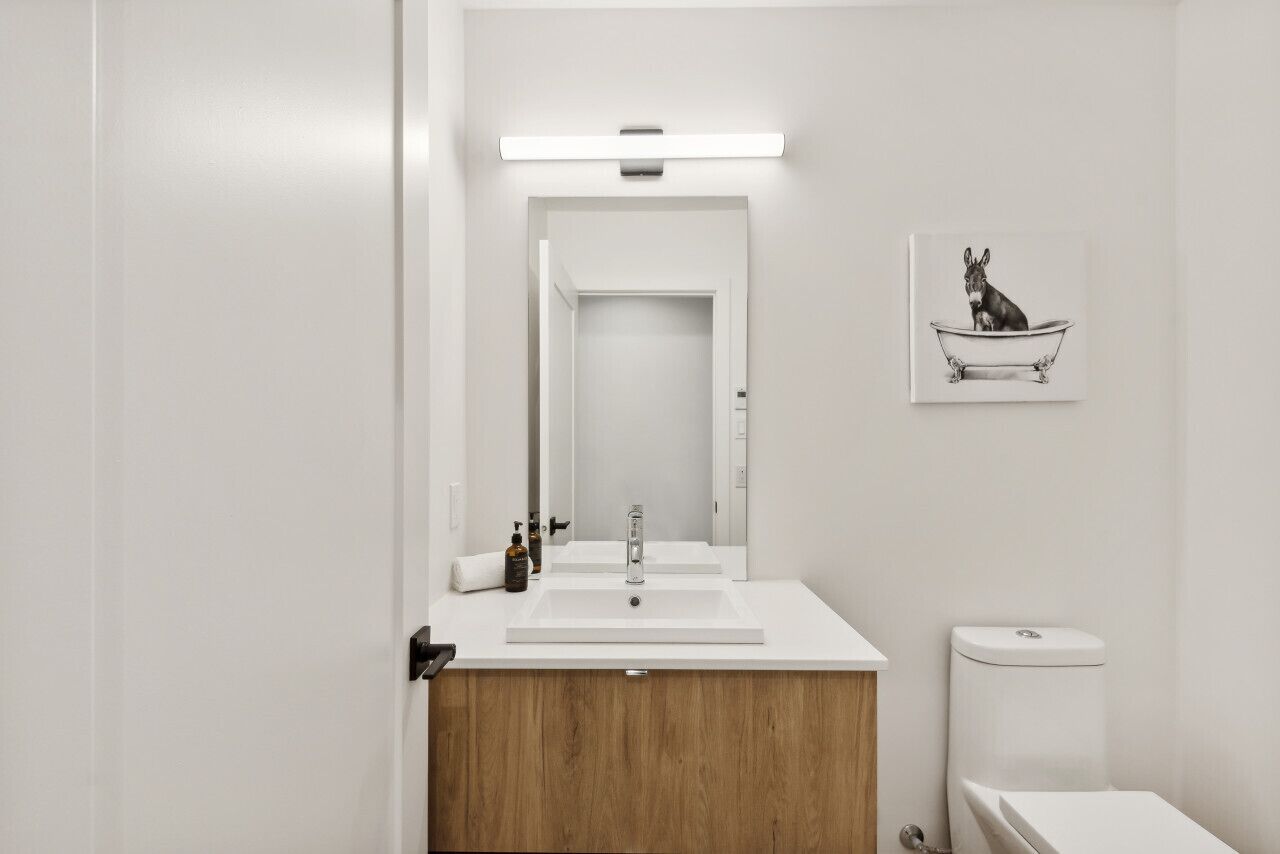 Un bany modern amb un lavabo blanc, un mirall, una aixeta i un vàter.