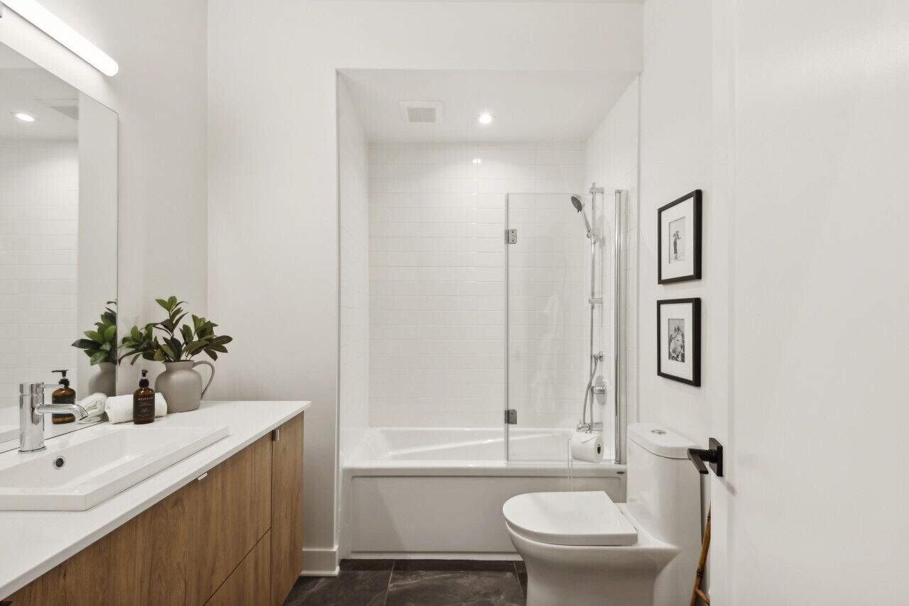 Ein modernes Badezimmer mit einem weißen Waschbecken, Spiegel und Toilette, einer Duschkabine und zwei gerahmten Bildern an der Wand.