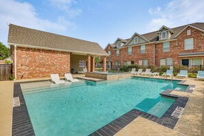 A swimming pool with lounge chairs, a covered patio, and brick buildings in the background. - Central College Station Townhome w/ Community Pool (College Station)