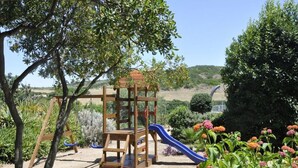 A playground with a slide and climbing structure surrounded by greenery and flowers. - Lubagnu Vacanze (Castelsardo)