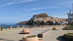 A coastal town with a historic fort on a hill, a paved promenade with planters, and a clear view of the sea. - Lubagnu Vacanze (Castelsardo)