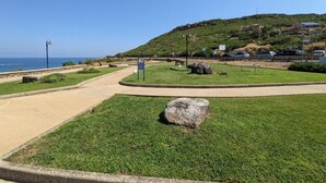 A coastal park with a paved walkway, grassy areas, and a large rock. - Lubagnu Vacanze (Castelsardo)