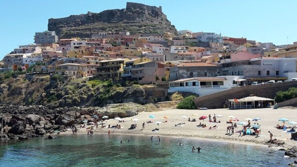 A coastal town with a rocky beach, clear water, and buildings with balconies overlooking the sea. - Lubagnu Vacanze (Castelsardo)