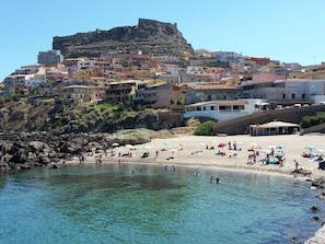 A coastal town with a rocky beach, clear water, and buildings with balconies overlooking the sea. - Lubagnu Vacanze (Castelsardo)