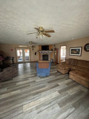 A spacious living room with a wooden floor, a ceiling fan, a fireplace, and a couch. - 2-bedroom vacation home minutes away from Greencastle and Depauw campus (Greencastle)