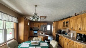 Une cuisine spacieuse avec des meubles de rangement en bois, une table à manger avec des chaises et un lustre.