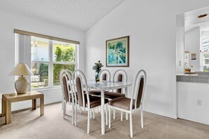 Ein Essbereich mit einem runden Tisch, sechs Stühlen, einer Lampe und einem Fenster mit Blick auf Grünflächen.