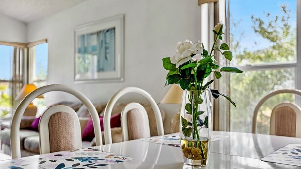 Un tavolo da pranzo con un vaso di fiori bianchi e una candela, circondato da sedie con schienale imbottito.