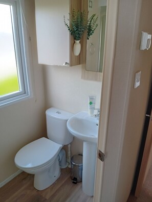 A compact bathroom with a toilet, sink, and a small trash bin.