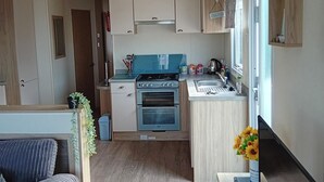A compact kitchen with a stove, oven, and sink. There is a small dining area with a sofa and a plant. - Seaside Chalet Retreat in New Quay (New Quay)