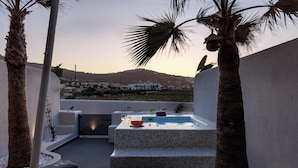 A rooftop terrace with a hot tub, seating area, and a view of a distant town.