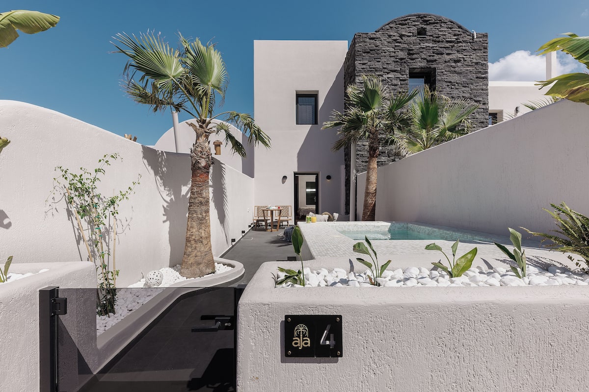 A modern building with a stone facade, a pool area with white pebbles, and palm trees.