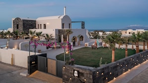 A modern building with a stone facade, a grassy courtyard, and a view of the sea.