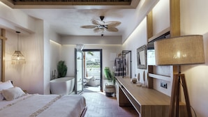 A modern bedroom with a bed, a ceiling fan, a vanity with a mirror, and a view to the outside.