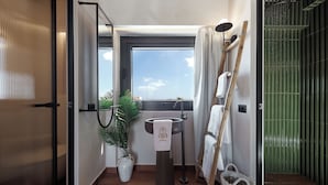 A modern bathroom with a large window, a sink, a potted plant, and a towel rack.