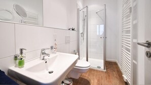 A modern bathroom with a white sink, toilet, and glass shower enclosure. - Haus Meeresloft - FW 3 (Norderney)