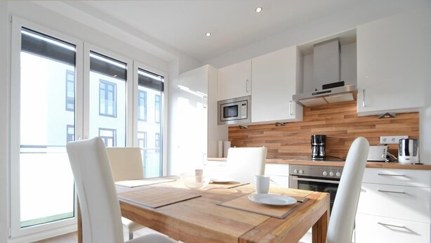A modern kitchen with white cabinets, a wooden countertop, and a built-in microwave. - Haus Meeresloft - FW 3 (Norderney)