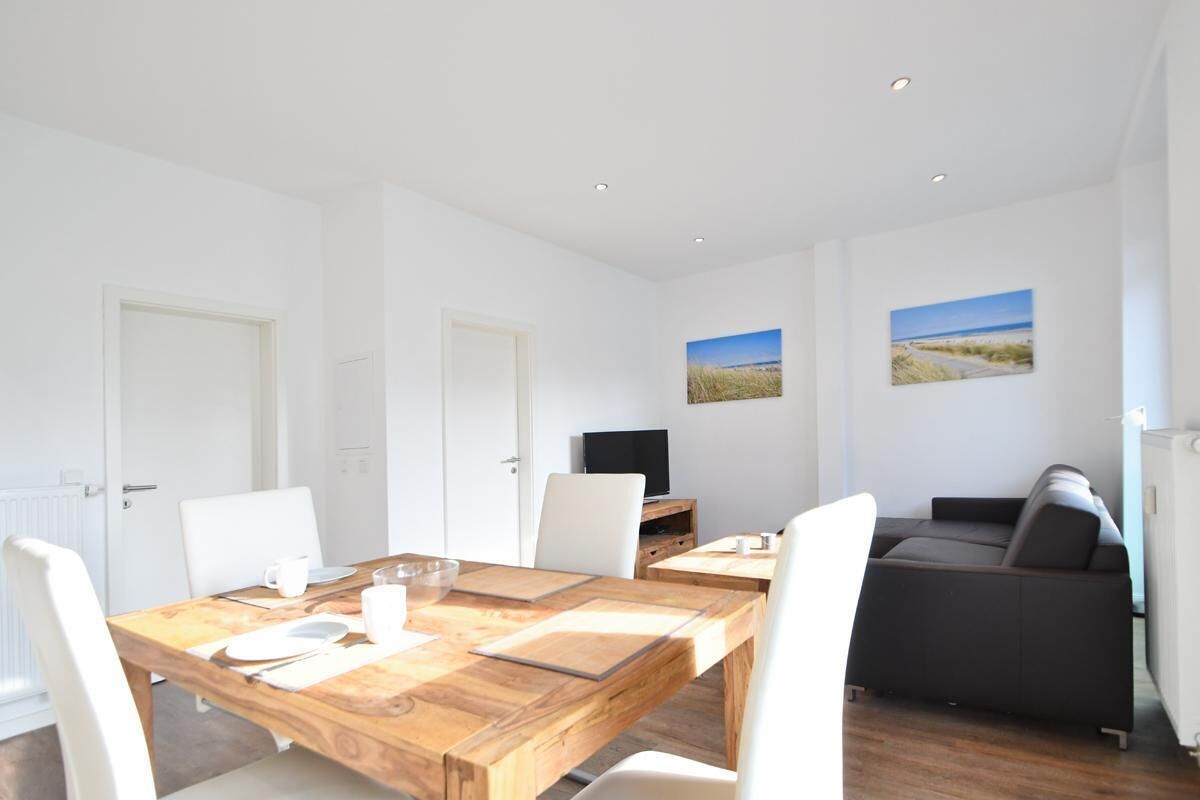 A modern room with a wooden dining table, white chairs, a dark sofa, and two framed pictures on the wall.