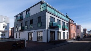 A modern multi-story building with large windows and balconies, situated on a street with other buildings. - Haus Meeresloft - FW 3 (Norderney)